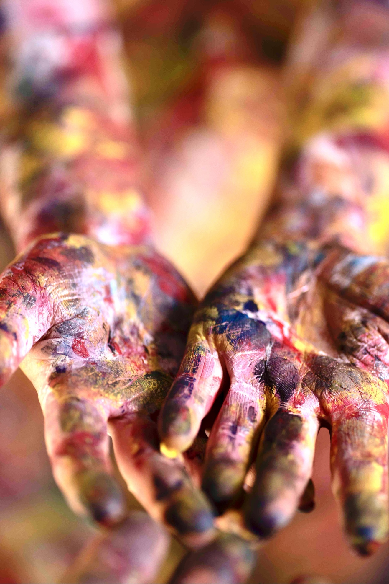 Paint-covered hands reaching toward the viewer in warm light